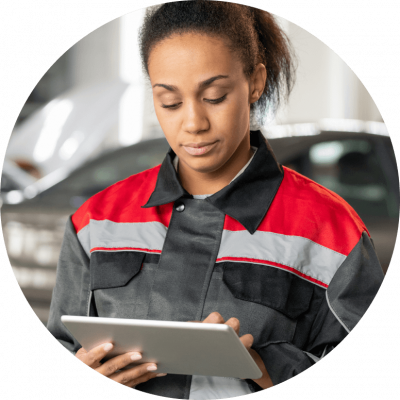 Black woman in black, red, and gray jacket works on a tablet in a car shop.